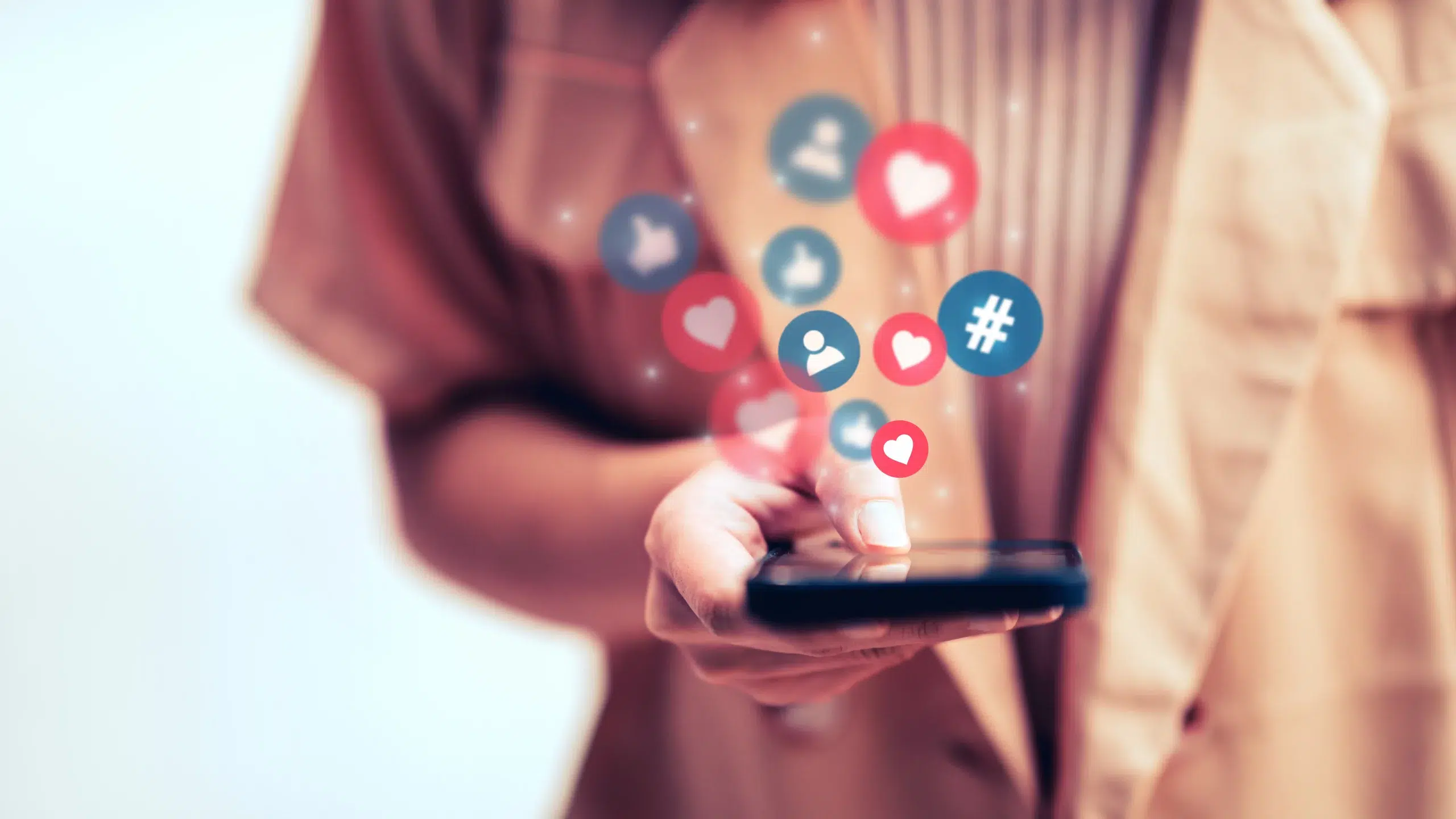 Persona sosteniendo un móvil del que salen iconos de likes, seguidores y hashtags
